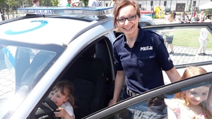 Uśmiechnięta dziewczynka siedzi w radiowozie policyjnym, obok stoi policjantka