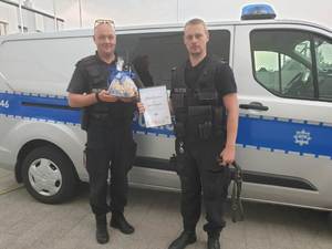 Dwóch policjantów z pisemnym podziękowaniem od dzieci stoi przed radiowozem