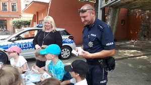 Policjant, dzieci i w tle radiowóz policyjny