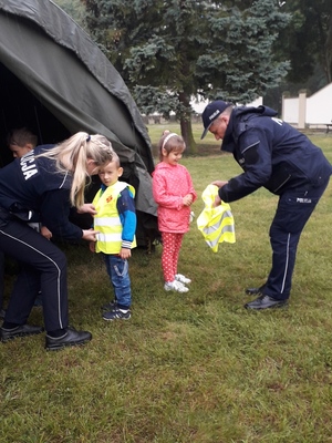 Pierwszy Zastępca Komendanta Miejskiego Policji w Toruniu i policjantka zakładają dzieciom kamizelki odblaskowe