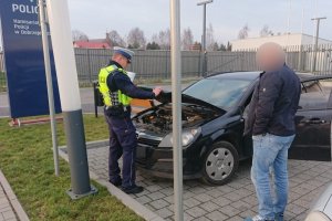 policjant kontroluje auto na parkingu przed komisariatem